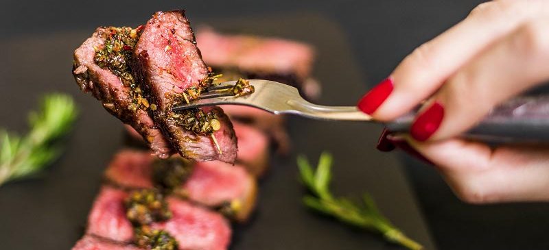 Une femme prend un morceau de viande rouge avec une fourchette