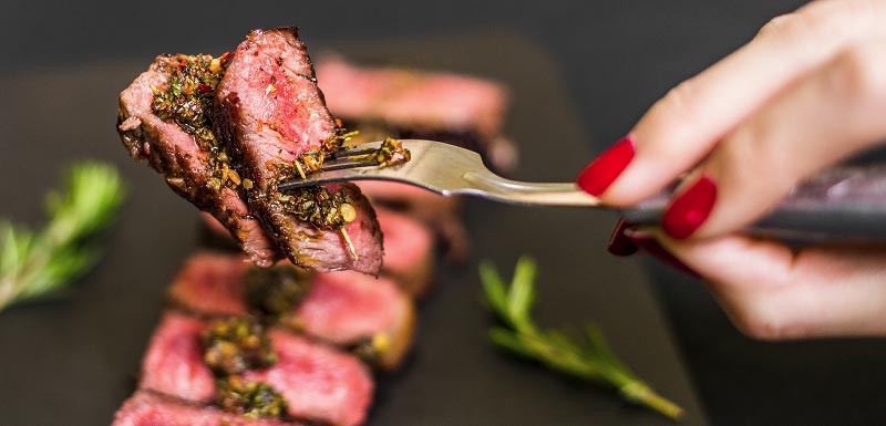 Une femme prend un morceau de viande rouge avec une fourchette