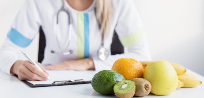 Une nutritionniste écrit la prescription destinée à un ealimentation saine sur un bureau avec des fruits