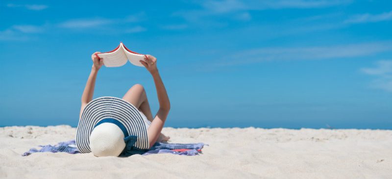 une femme est entrain de lire, allongée sur la plage