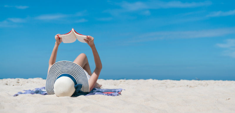 une femme est entrain de lire, allongée sur la plage