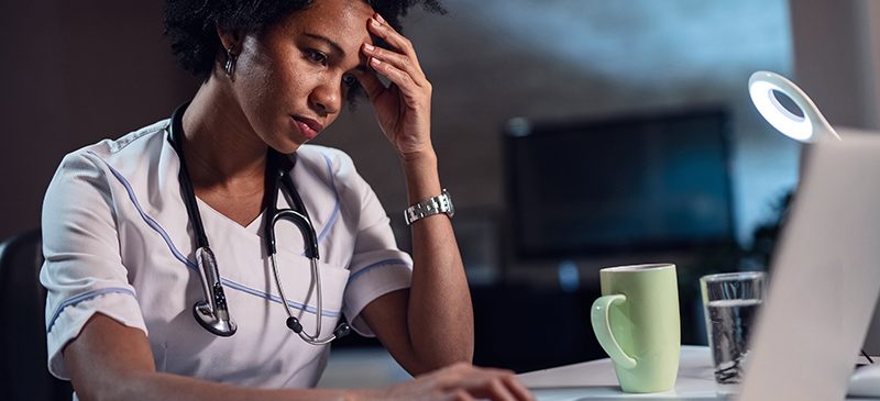 Médecin femme afro-américaine avec maux de tête travaillant la nuit sur son ordinateur portable