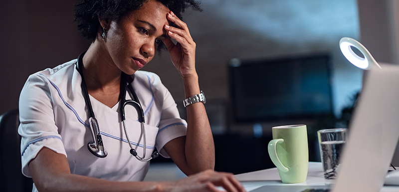 Médecin femme afro-américaine avec maux de tête travaillant la nuit sur son ordinateur portable