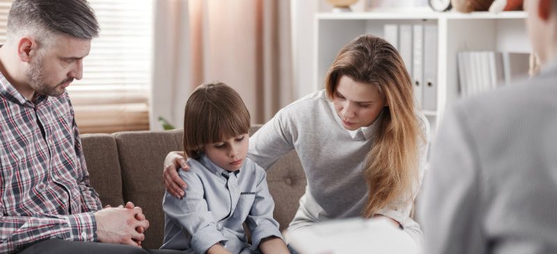 Mère embrassant son fifls autiste, assise à côté de son père pendant une thérapie familiale