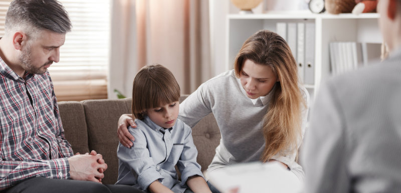 Mère embrassant son fifls autiste, assise à côté de son père pendant une thérapie familiale