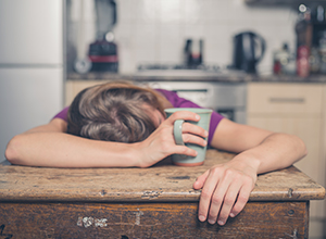 Femme fatigué à cause du stress et allongé sur la table de la cuisine avec une tasse de thé dans la main