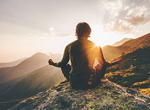 Homme faisant du yoga et de la médiation sur un flanc de montagne devant un coucher de soleil à cause du stress