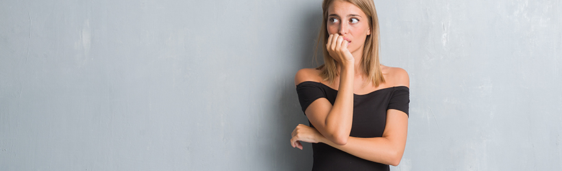 belle jeune femme élégante avec une robe grunge debout devant le mur gris qui est en stress car elle ronge ses ongles