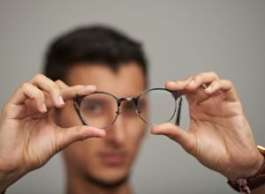 Homme qui tient sa paire de lunettes dans ses deux mains devant lui