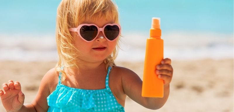 Petite fille qui joue avec un tube de crème solaire