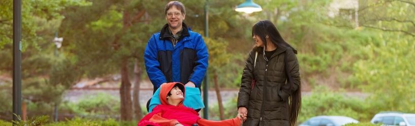 Enfant handicapé dans un fauteuil roulant poussé par son père et sa soeur