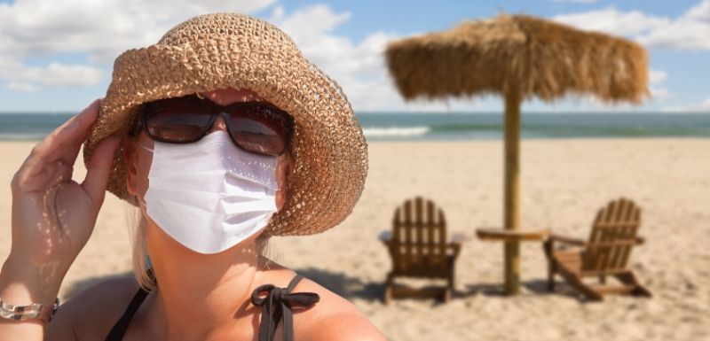 Femme qui porte son masque à la plage, avec chapeau, lunettes de soleil