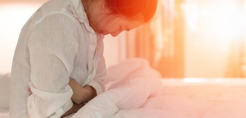 Femme assise dans son lit qui a mal au ventre