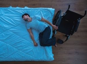 homme qui est allongé sur le lit, son fauteur roulant se trouve à côté de lui