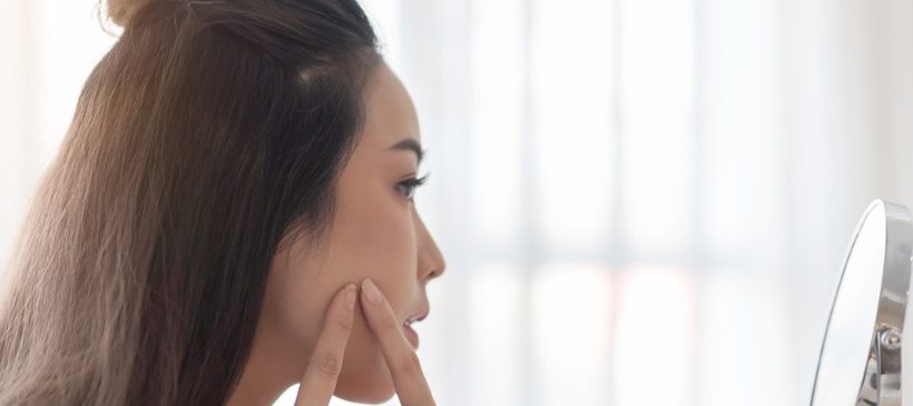 Une femme touchant un bouton d'acné devant un miroir