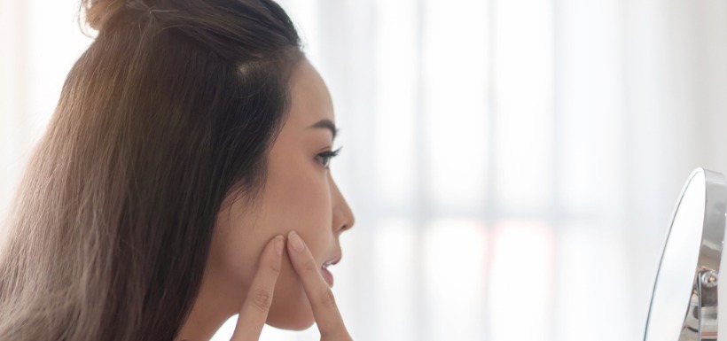 Une femme touchant un bouton d'acné devant un miroir 