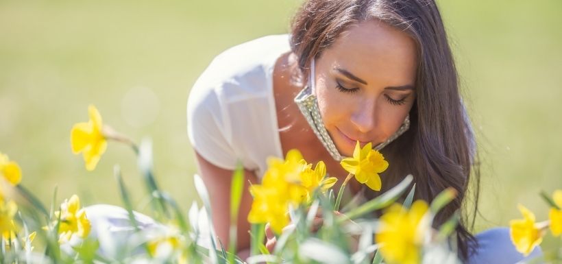 Femme qui sent l'odeurs des fleur, portant son masque en tissus sous le menton