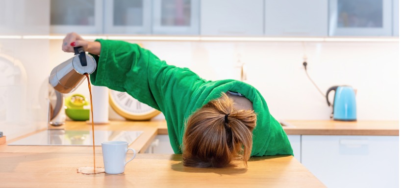 femme avec la tête contre le plan de travail se servant du café a coté de sa tasse 