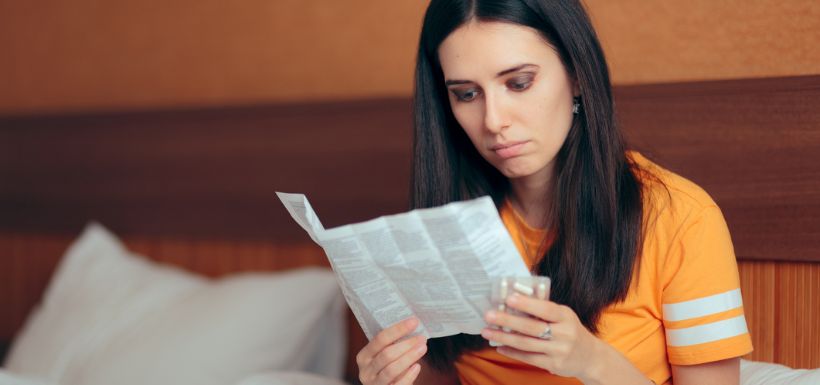 Une femme lit la notice de ces médicaments qui indiquent comment les prendre et les conserver.