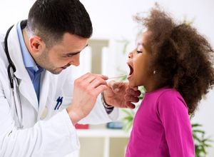 Photo d'un docteur qui fait tirer la langue à un enfant pour voir sa stomatite.